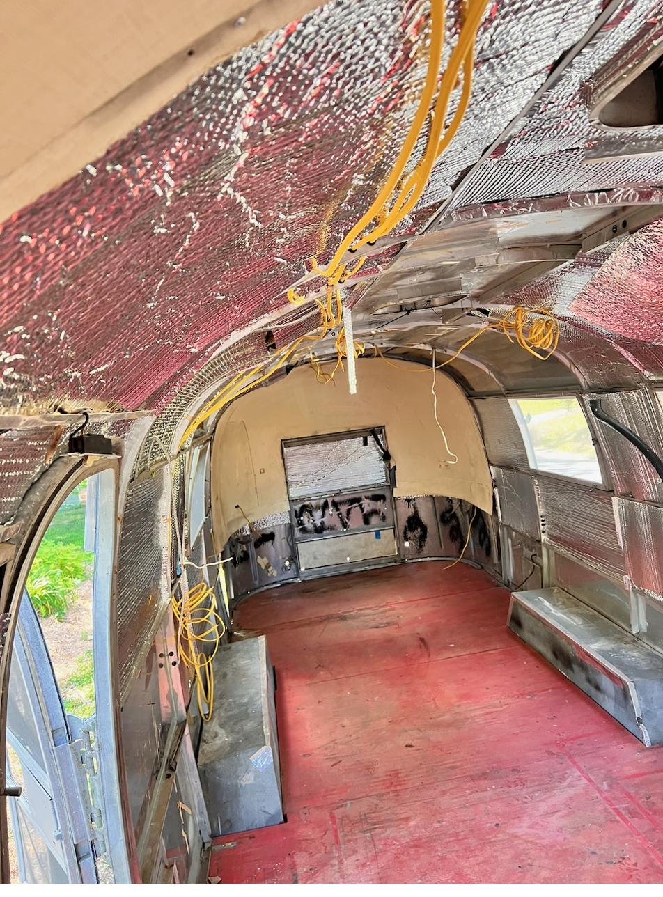 Interior of the Silver Bullet Airstream looking up at the curved ceiling ribs and insulation, with yellow wiring running overhead.