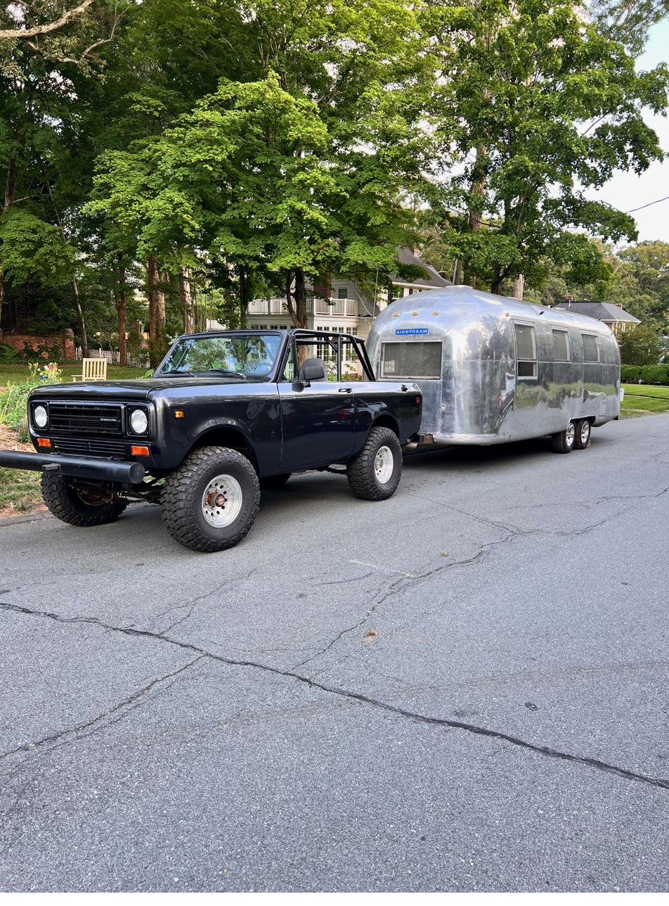 The Scout towing the Silver Bullet Airstream down a tree-lined street in the evening light.