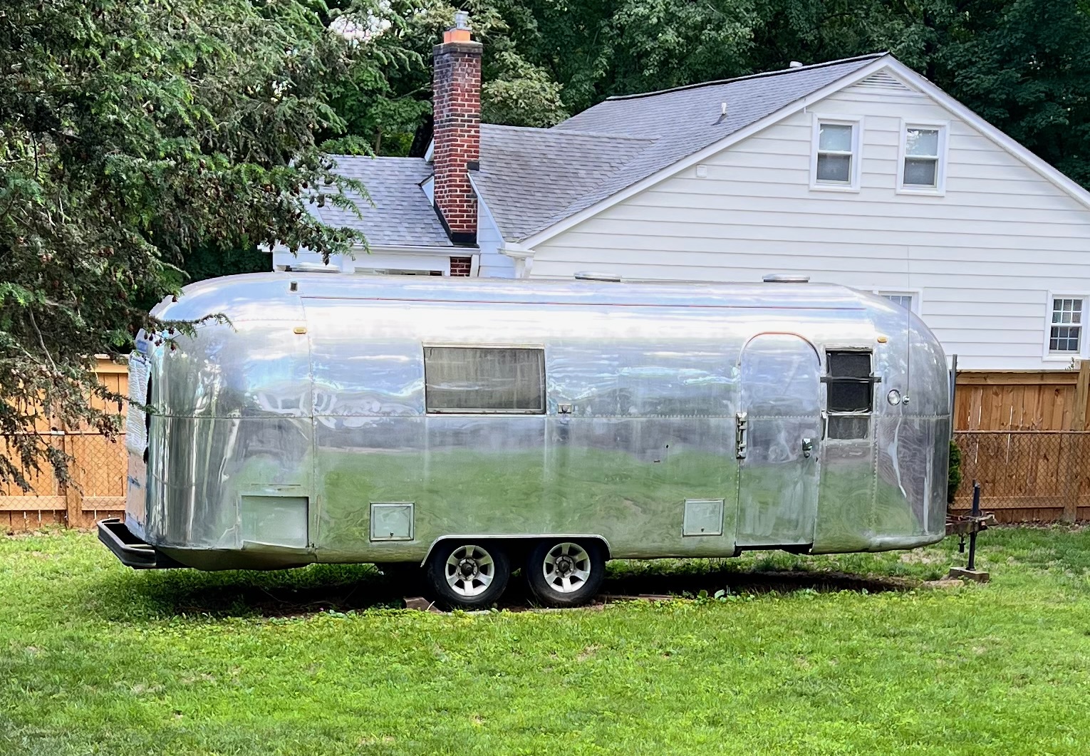 Full side view of the polished Silver Bullet Airstream parked on the grass in a fenced backyard.